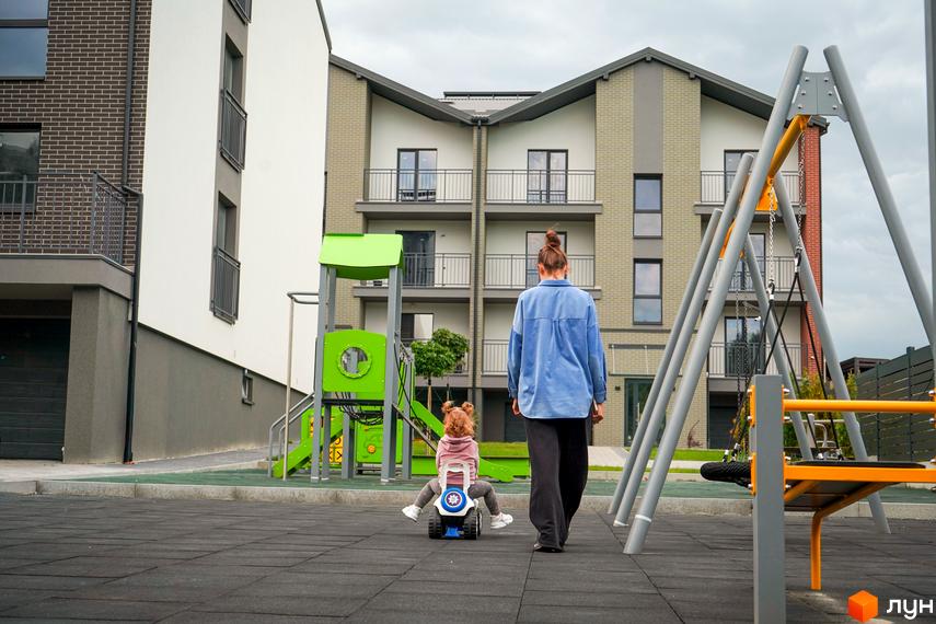 Житловий комплекс Вілла Швейцарія: фасади будинків з балконами та дитячий майданчик з гойдалкою та гіркою.