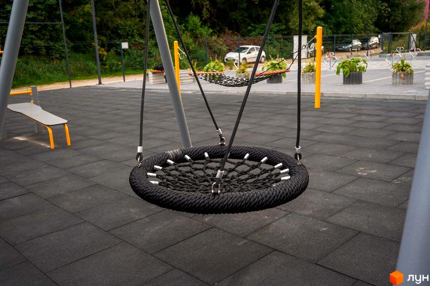 Дитячий майданчик з гойдалкою-гніздом та лавкою в ЖК Вілла Швейцарія. Територія комплексу облаштована для відпочинку.
