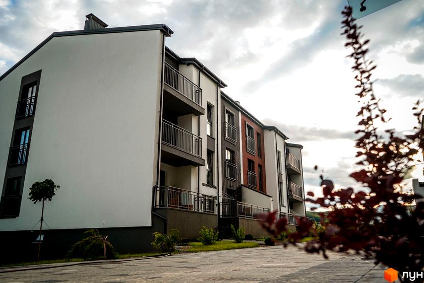 Зовнішній вигляд новобудови ЖК Вілла Швейцарія з балконами та цегляними елементами фасаду, прибудинкова територія з деревами та газоном.