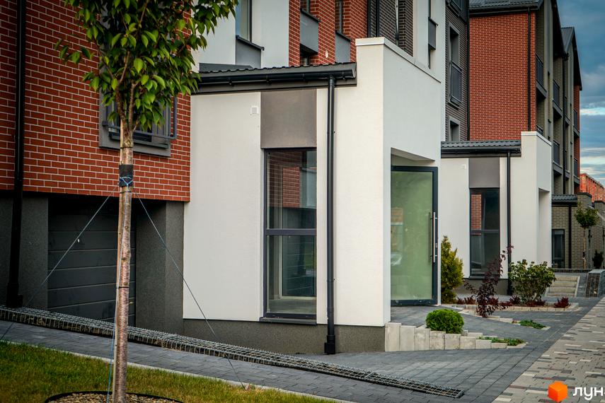 Житловий комплекс Вілла Швейцарія: фасади будинків з червоної цегли та білої штукатурки, доглянута прибудинкова територія з бруківкою та зеленими насадженнями.