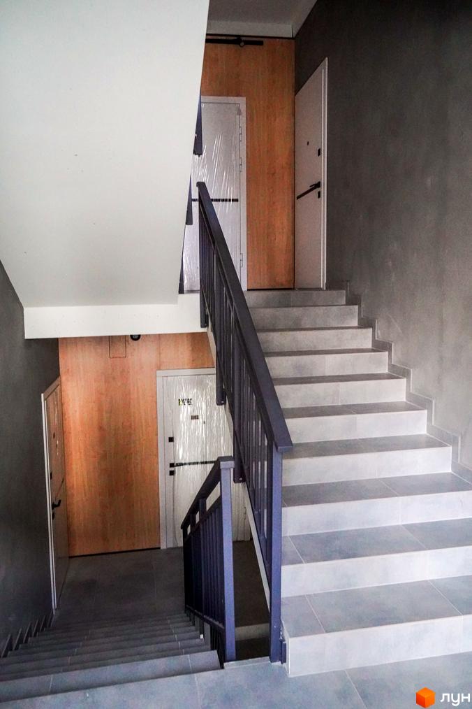 Сходи та двері в новобудові ЖК Вілла Швейцарія. Внутрішній вигляд сходової клітки з сірими стінами та дерев'яними елементами.