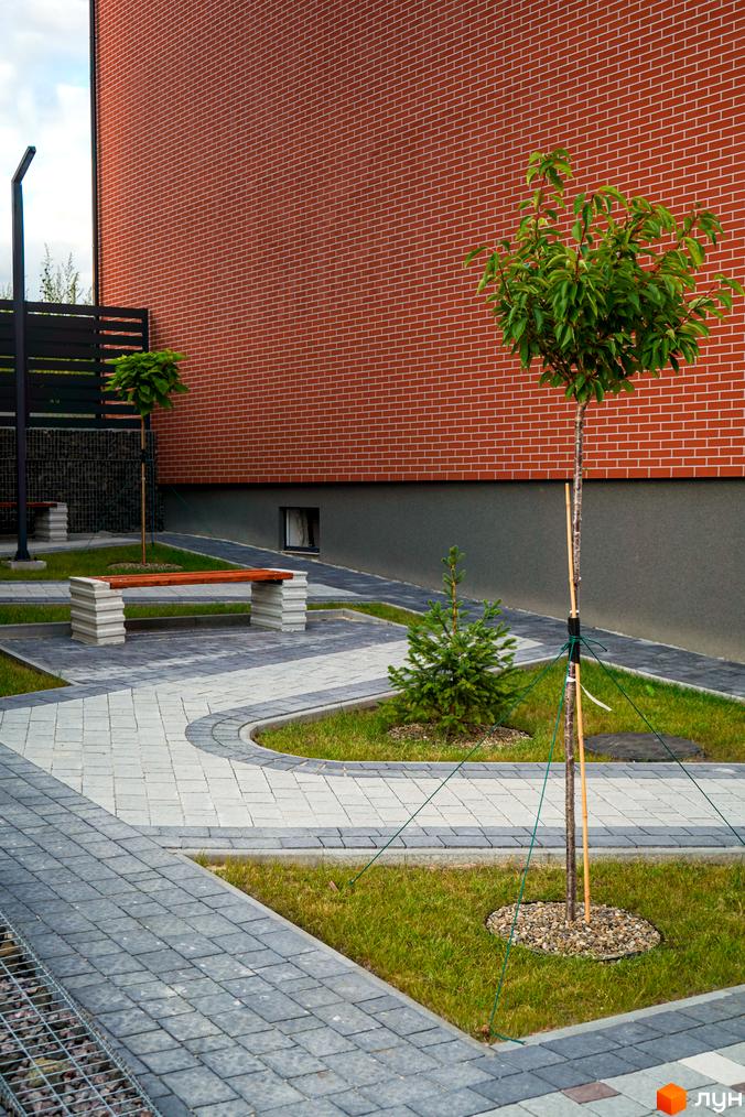 Новобудова ЖК Вілла Швейцарія з цегляним фасадом та доглянутою прибудинковою територією з бруківкою та деревами.