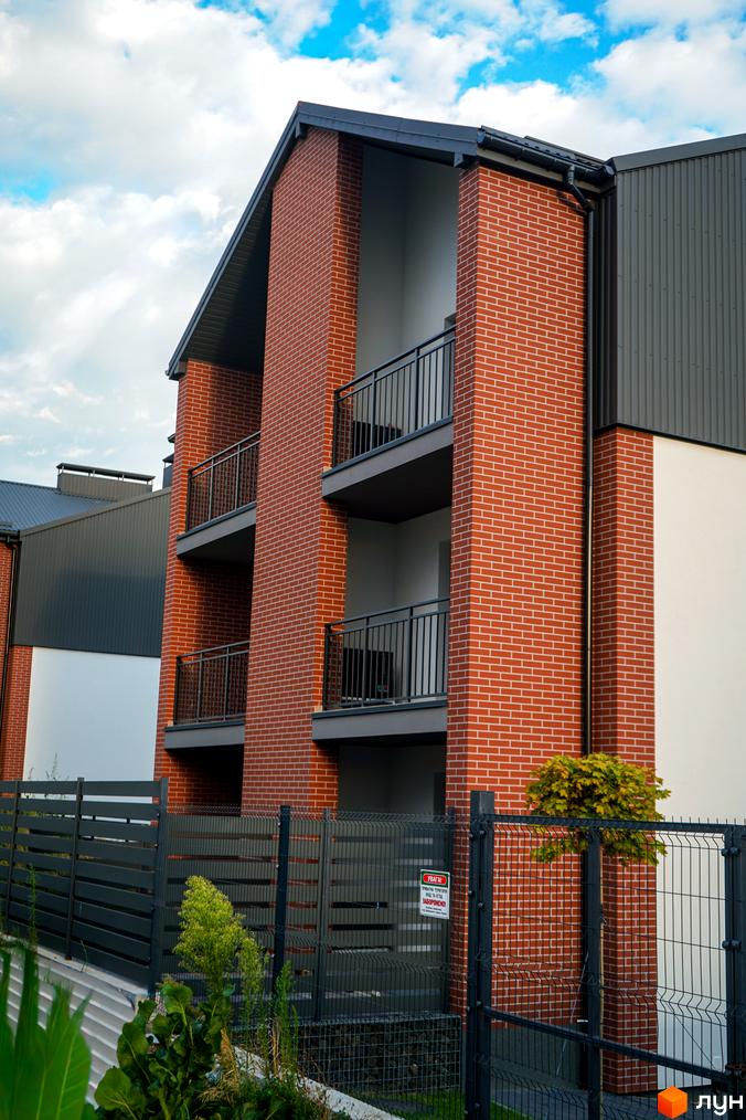 Новобудова ЖК Вілла Швейцарія з червоної цегли та сірим фасадом, огороджена парканом. Зовнішній вигляд будинку та прибудинкової території.