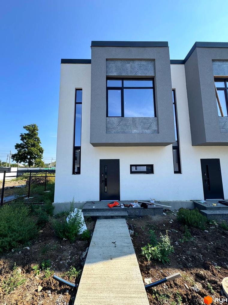 Зовнішній вигляд таунхаусів 11Dreams з великими вікнами та сірими елементами фасаду. Навколо будівельний майданчик з деревами та огорожею.