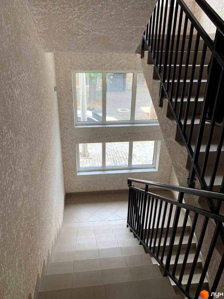 Сходи в ЖК Будинок на Маланова з вікнами, що виходять на бруківку та дерева. Зовнішній вигляд новобудови.