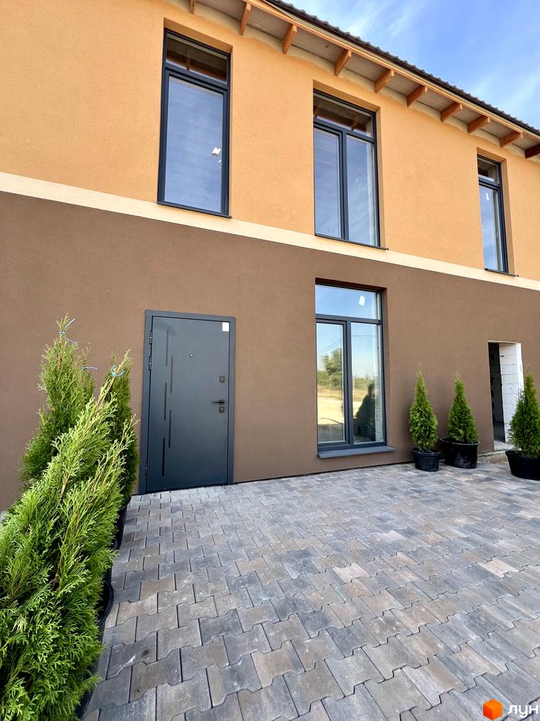 Таунхауси Лісовий затишок: двоповерховий будинок з коричневим та помаранчевим фасадом, великими вікнами та вимощеною плиткою прибудинковою територією.