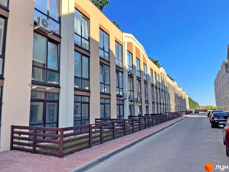 Зовнішній вигляд житлового комплексу Smart Residence з великими вікнами та індивідуальними кондиціонерами. Прибудинкова територія з дерев'яною огорожею та бруківкою.