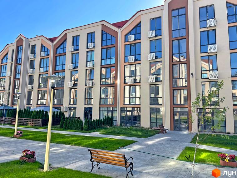 Фасад новобудови ЖК Smart Residence з великими вікнами та кондиціонерами. Поруч доглянута прибудинкова територія із зеленими насадженнями та лавкою.