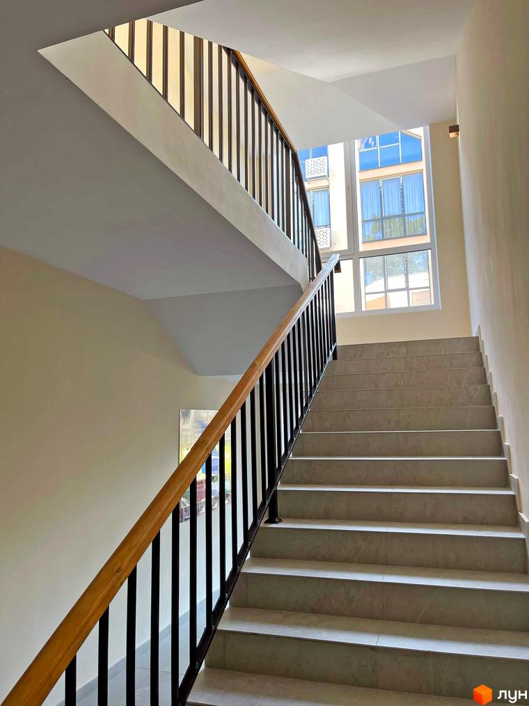 Фото сходової клітини в новобудові ЖК Smart Residence з великими вікнами та плиткою на сходах. Зовнішній вигляд будинку з вікнами та балконами.