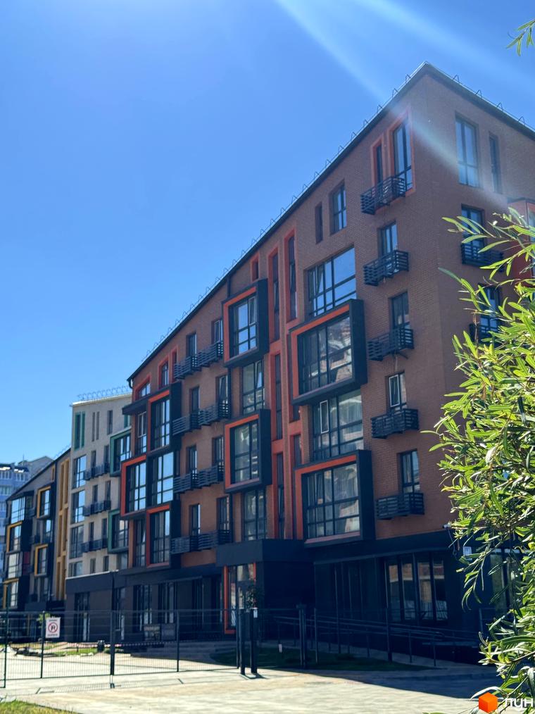 Фасад житлового комплексу Verba з цегляним оздобленням та яскравими акцентами, вікна та балкони, прибудинкова територія з огорожею.