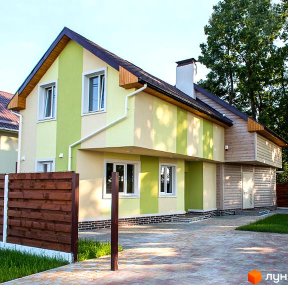 Зображення двоповерхового будинку в Котеджному містечку Garden Street з зелено-бежевим фасадом та коричневим дахом. Перед будинком викладена бруківка та видно частину дерев'яного паркану.