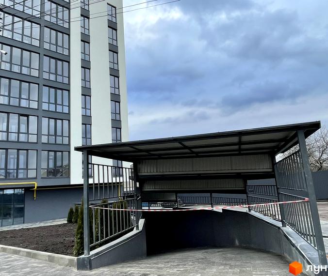 Зовнішній вигляд новобудови з великими вікнами та прибудинковою територією з навісом для паркування. Будівельний проєкт вул. Будівельна, 1.