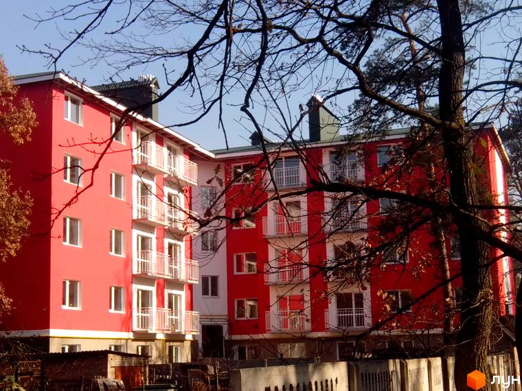 Зображення фасаду будинку по вул. Університетська, 34. Багатоповерхова будівля з балконами та червоними стінами на тлі дерев.