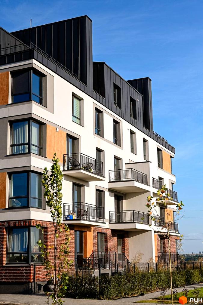Фасад житлового комплексу Haute Couture з цегляною та білою обробкою, балконами та великими вікнами. Навколо будинку зелені насадження та доглянута прибудинкова територія.