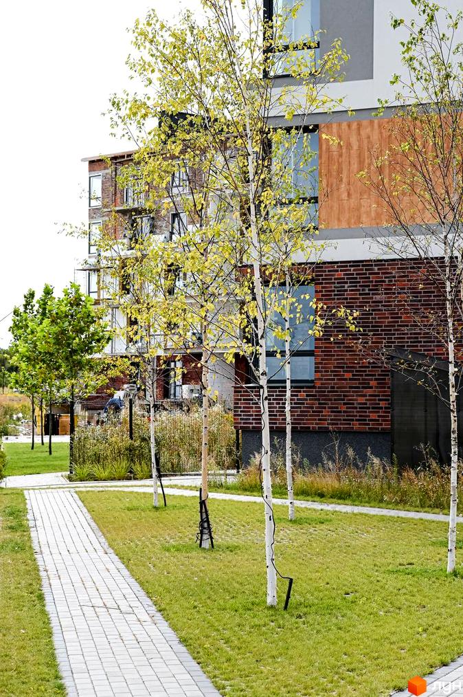 Новобудова ЖК Haute Couture з цегляним фасадом та скляними вікнами, поруч доглянута прибудинкова територія з доріжкою та газоном.