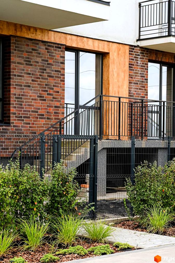 Новобудова ЖК Haute Couture з цегляним фасадом та дерев'яними елементами. Прибудинкова територія з огорожею та зеленими насадженнями.