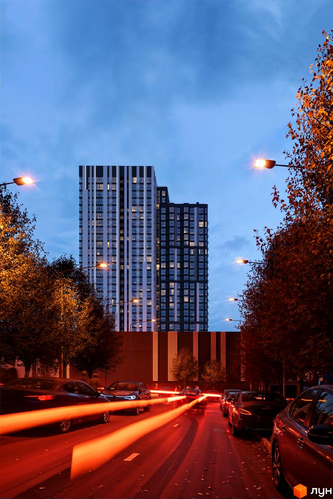 Житловий комплекс Avalon Up з фасадом у смужку та освітленою вулицею з автомобілями ввечері. Навколо багато дерев з осіннім листям.