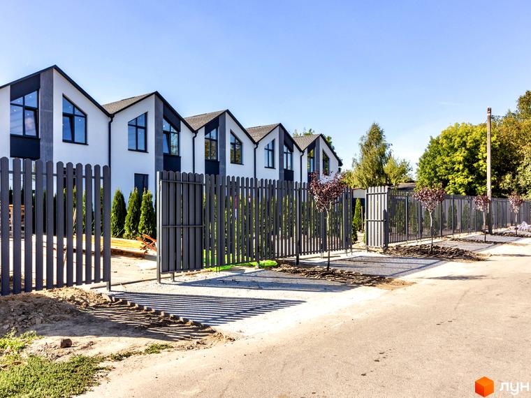 Таунхауси Small Town з біло-сірими фасадами та темними дахами, огороджені парканом. Поруч зелені насадження та дорога.