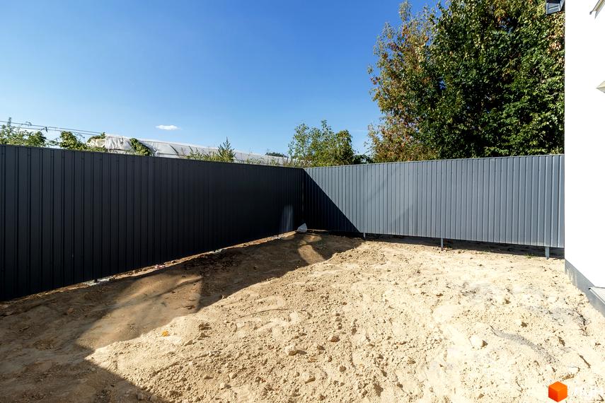 Таунхауси Small Town: огороджена територія з піщаним покриттям та парканом. Навколо зелені дерева та блакитне небо.