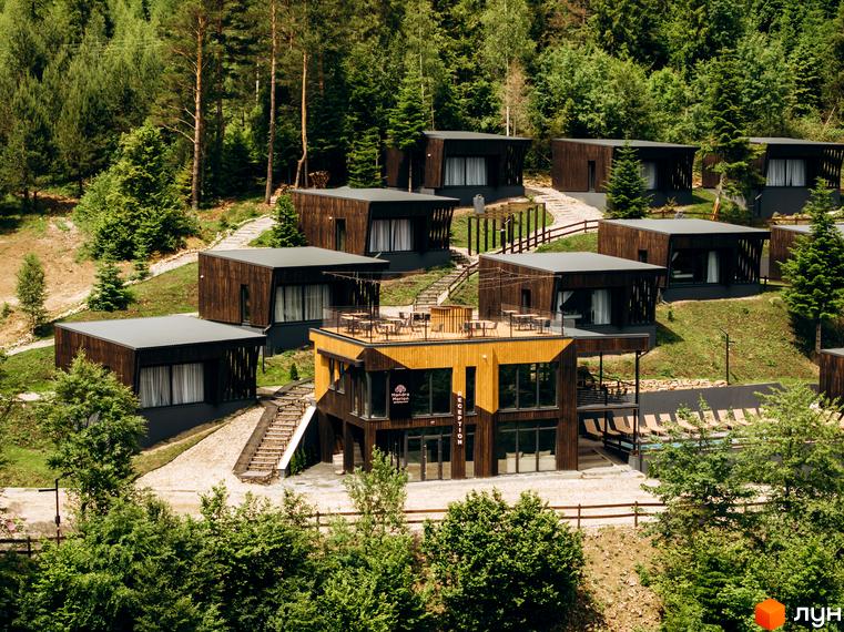 Котеджне містечко КМ Моріон: дерев'яні будинки на схилі гори серед лісу. Тераса з меблями, басейн та шезлонги на прибудинковій території.