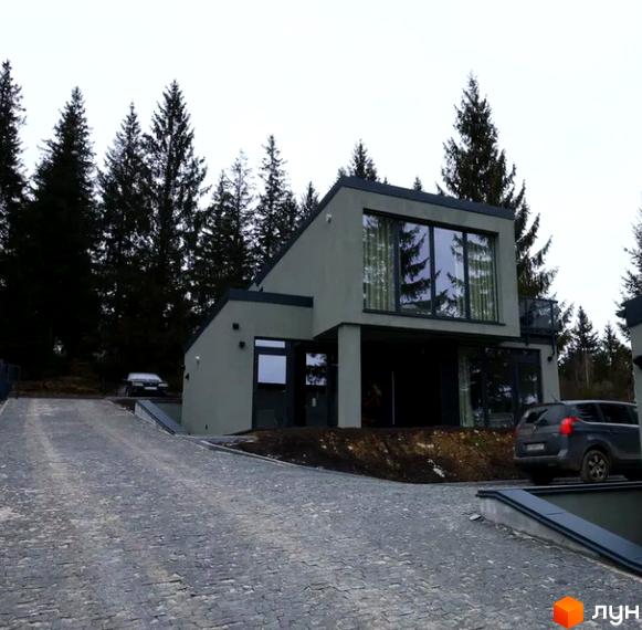 Котеджне містечко КМ Solomon Residence. Сучасний будинок з великими вікнами та сірою обробкою на тлі лісу, з бруківкою на подвір'ї та автомобілями.