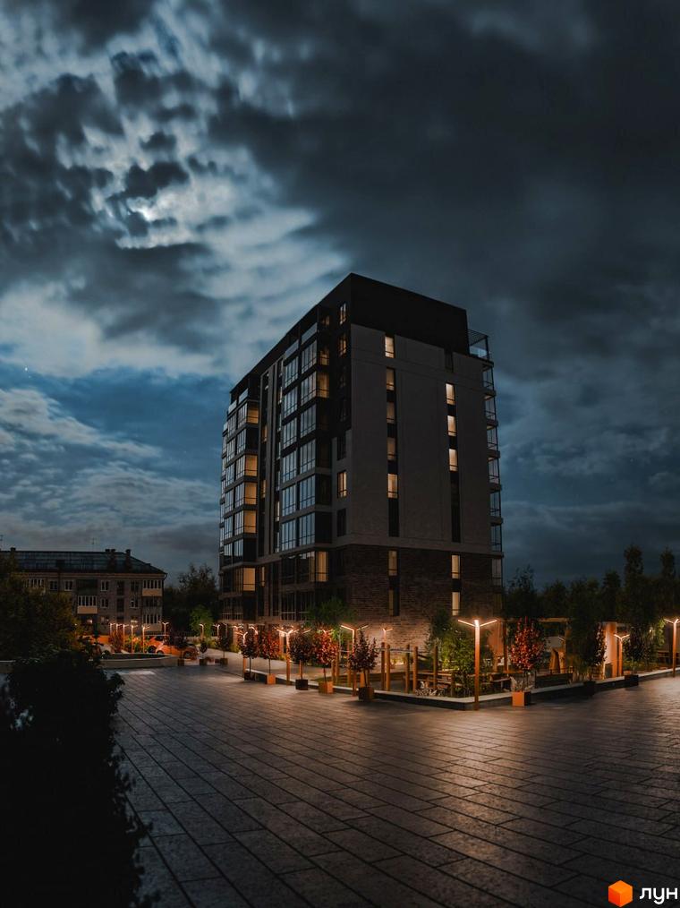 Житловий комплекс Перемога вночі. Багатоповерховий будинок з підсвіченими вікнами та освітленою прибудинковою територією з деревами та ліхтарями.