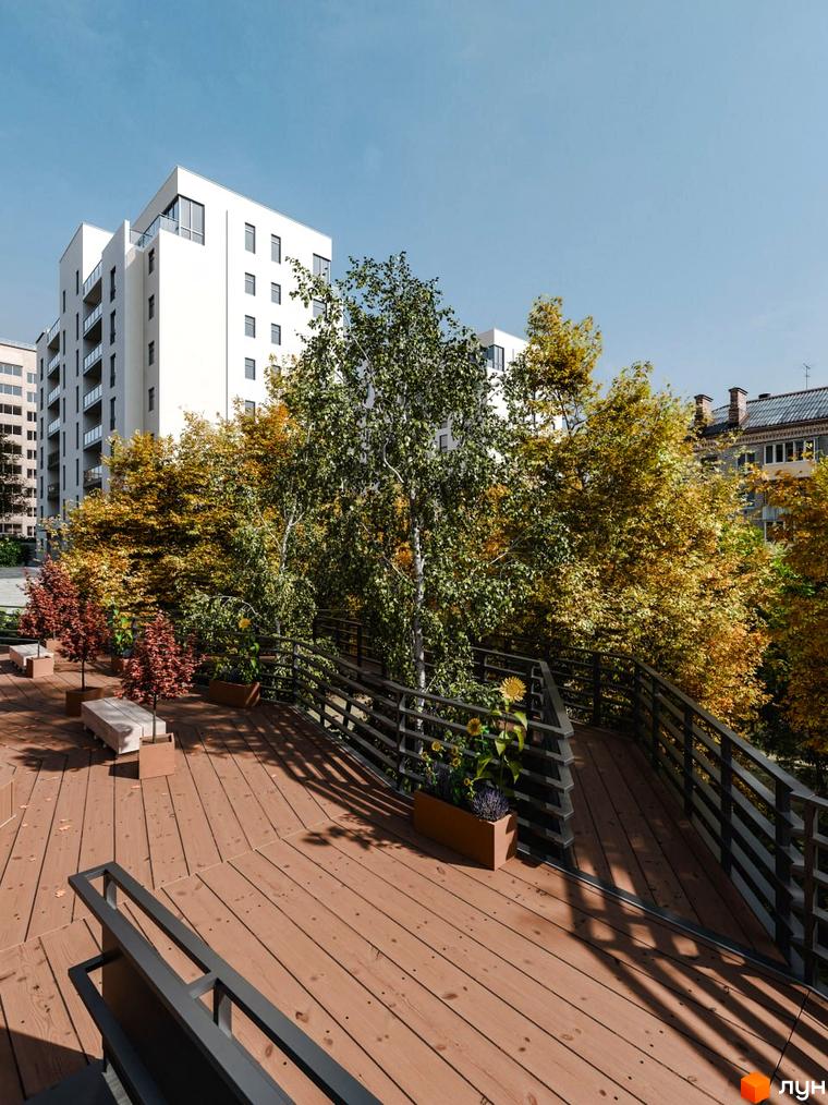 Житловий комплекс Перемога: біла багатоповерхівка з балконами та прибудинкова територія з дерев'яною терасою, лавками та деревами.