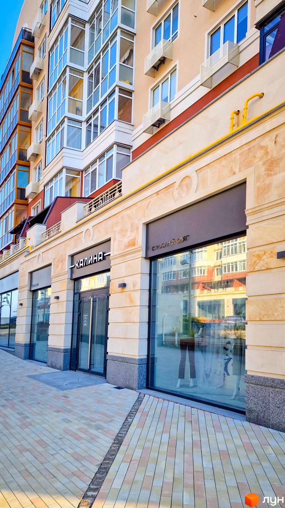 Фасад житлового комплексу Греків Ліс з комерційними приміщеннями на першому поверсі та вимощеною пішохідною зоною.