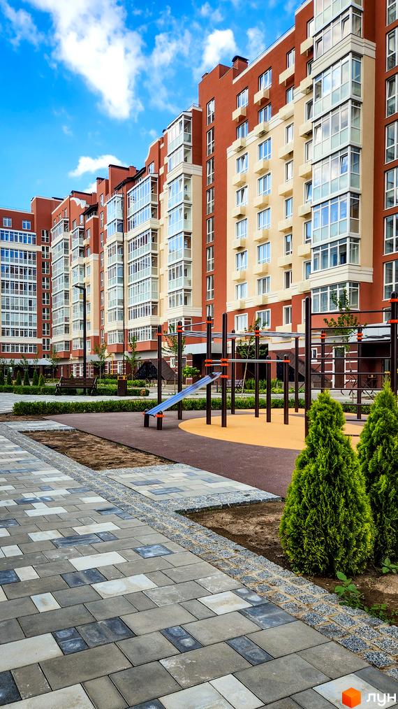Житловий комплекс Греків Ліс з червоно-бежевими фасадами та заскленими балконами, дитячим майданчиком та зеленими насадженнями.