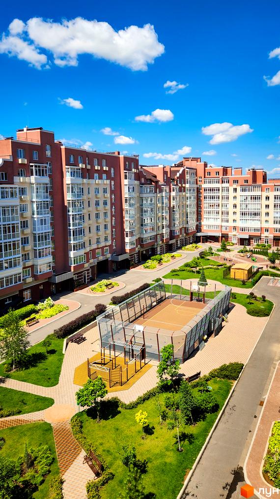 Житловий комплекс Греків Ліс з червоно-бежевими фасадами та великими вікнами, з баскетбольним майданчиком та зеленим двором.