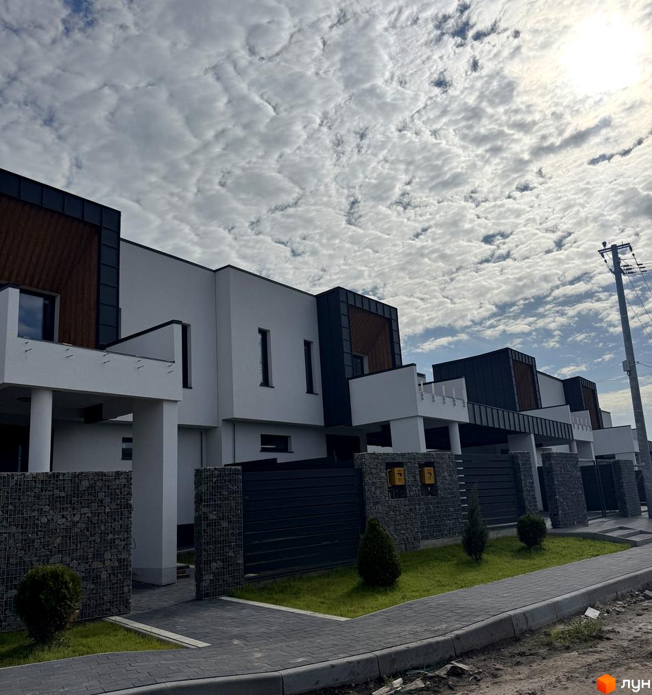 Котеджне містечко КМ Lake House Sokilnyky. Зовнішній вигляд будинків з білою штукатуркою, темними дахами та дерев'яними вставками. Прибудинкова територія з газоном та бруківкою.