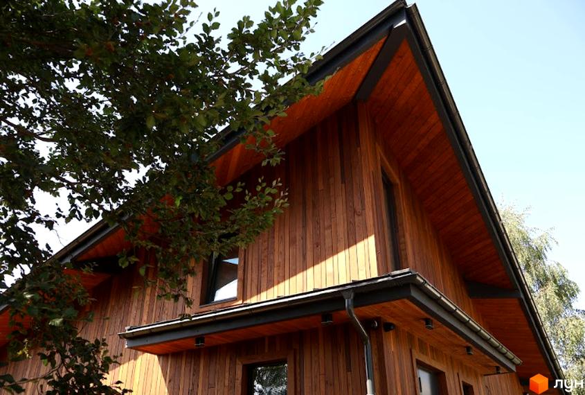 Котеджне містечко Тишагора: дерев'яний будинок з великими вікнами та навісом. Навколо зелені дерева.