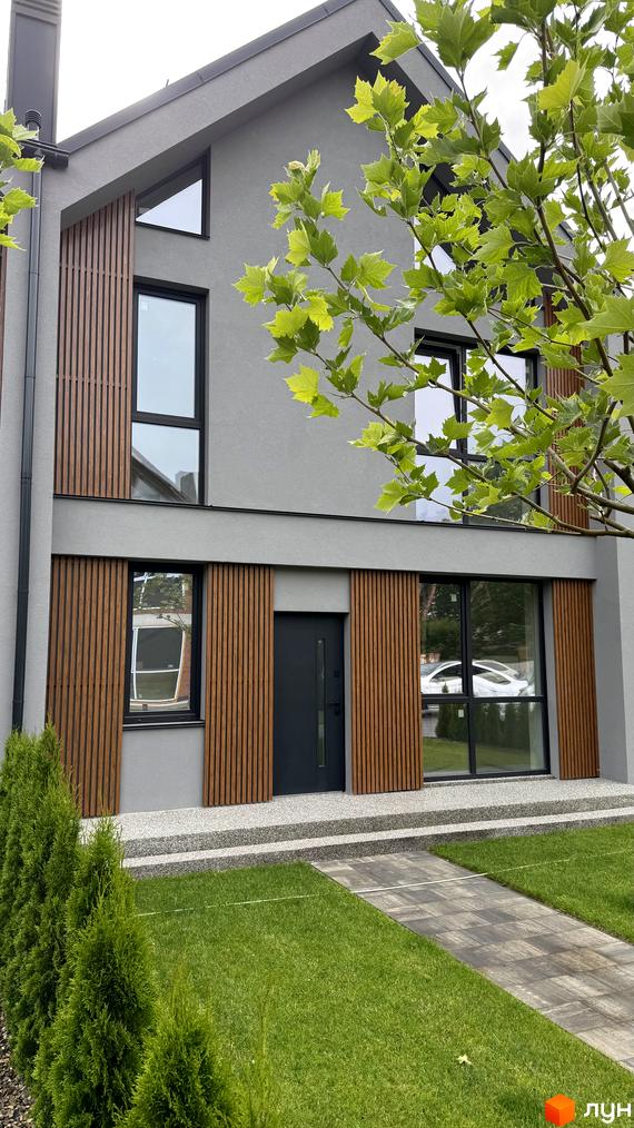 Таунхауси Legend Town з дерев'яними панелями та великими вікнами. Перед будинком доглянутий газон та доріжка.