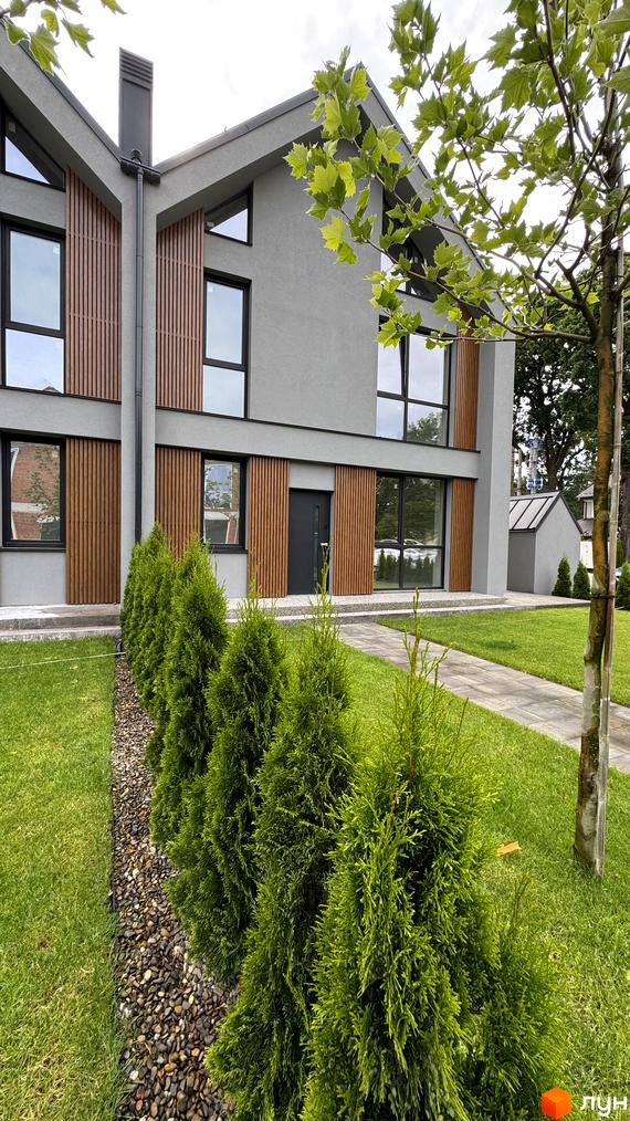 Таунхауси Legend Town з сірим фасадом та дерев'яними вставками, доглянута прибудинкова територія з газоном та туями.