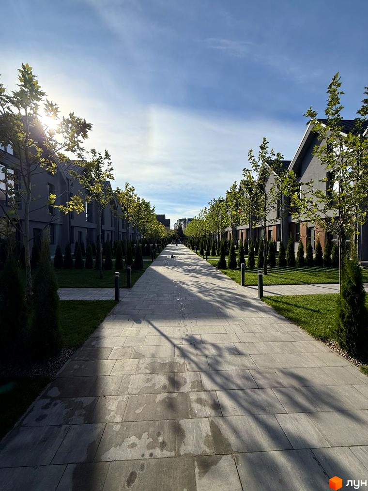 Legend Town таунхауси з сірими фасадами та темними дахами, упорядкована прибудинкова територія з доглянутими газонами та деревами.