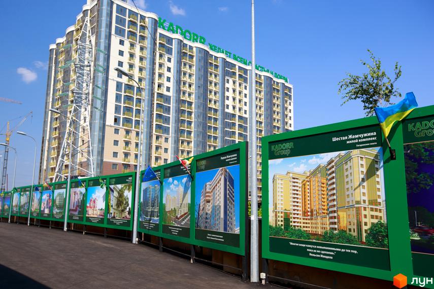 Житловий комплекс Третья Жемчужина з сучасним фасадом та прибудинковою територією, огороджений рекламними щитами.