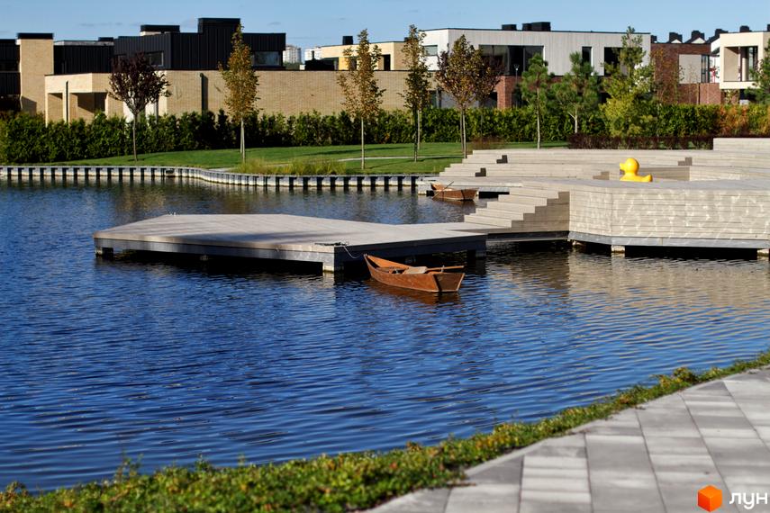 Котеджне містечко О.Краса: сучасні будинки та зона відпочинку біля води з човнами. Комплекс розташований біля озера з дерев'яними настилами та ландшафтним дизайном.