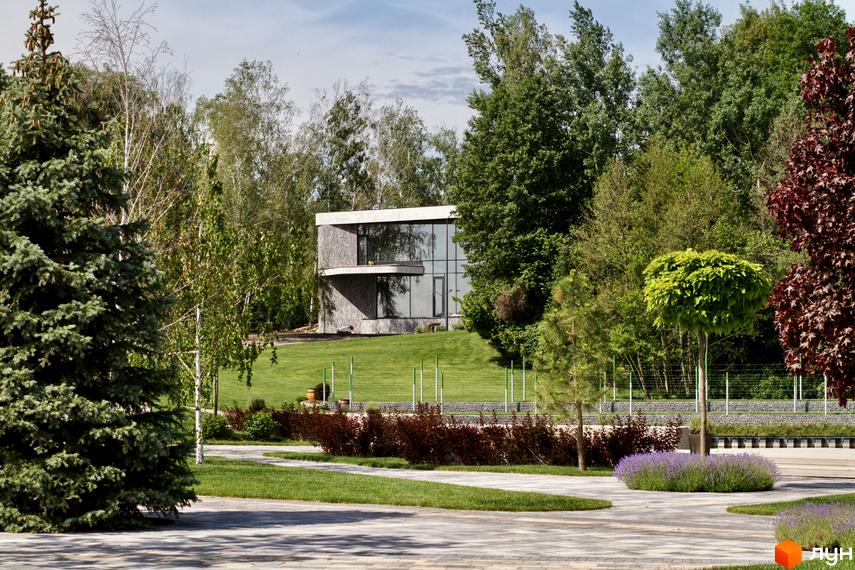 Котеджне містечко О.Краса: двоповерховий будинок з панорамними вікнами на фоні зелених дерев та доглянутої прибудинкової території.