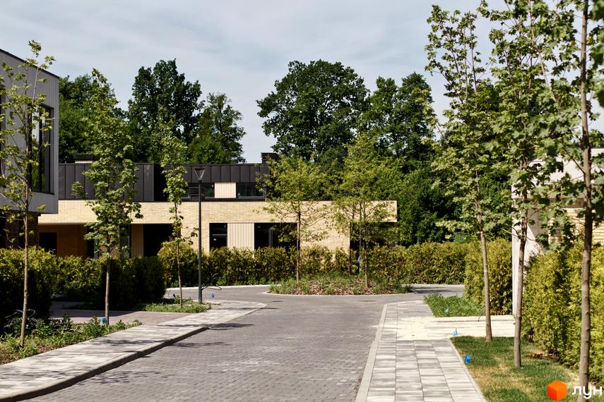 Котеджне містечко О.Краса: цегляні будинки з темними дахами та великими вікнами, оточені зеленню та вимощеними доріжками.