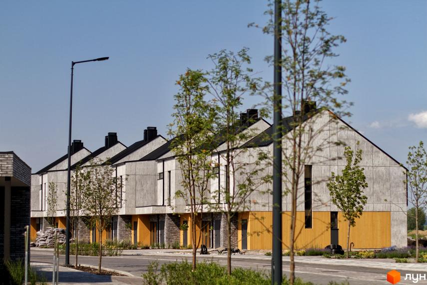 Котеджне містечко О.Краса: сучасні будинки з сірими фасадами та жовтими вставками, зелені дерева та доглянута прибудинкова територія.