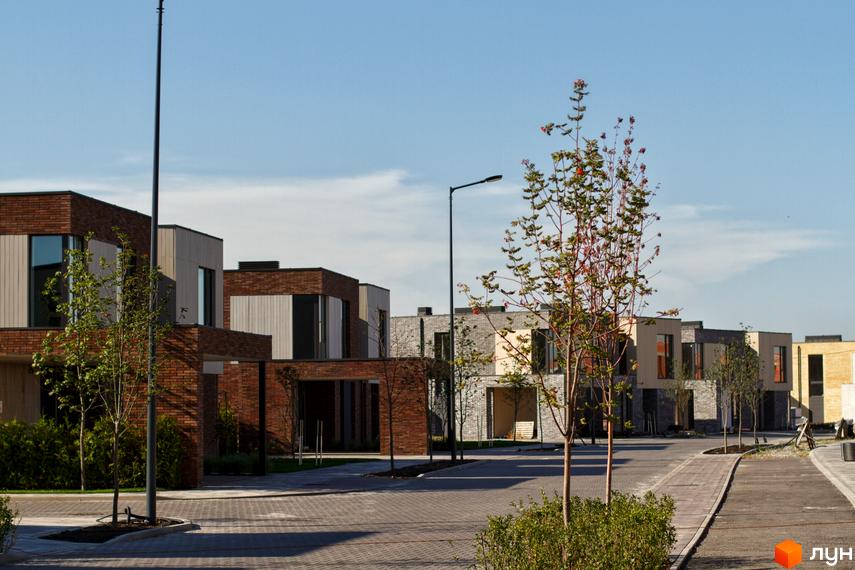 Котеджне містечко О.Краса: фасади будинків з цегли та дерева, брукована вулиця та зелені насадження. Сучасна архітектура та доглянута територія.