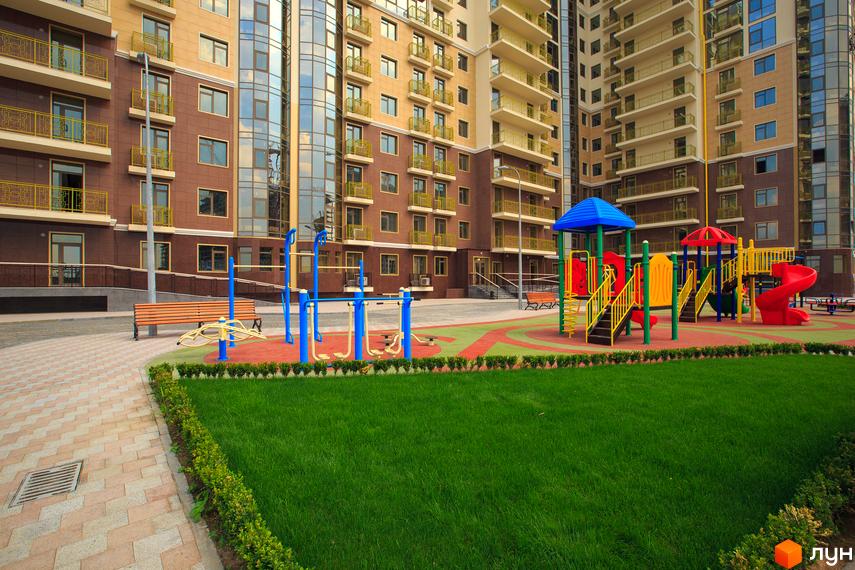 Житловий комплекс Третья Жемчужина з сучасним фасадом та прибудинковою територією, облаштованою дитячим майданчиком.