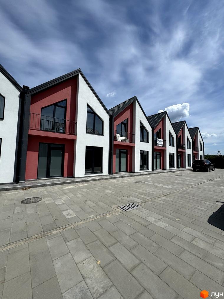 Таунхауси Freya – фасади будинків з червоними та білими елементами, великими вікнами та чорними дахами. Поруч – вимощена плиткою прибудинкова територія.