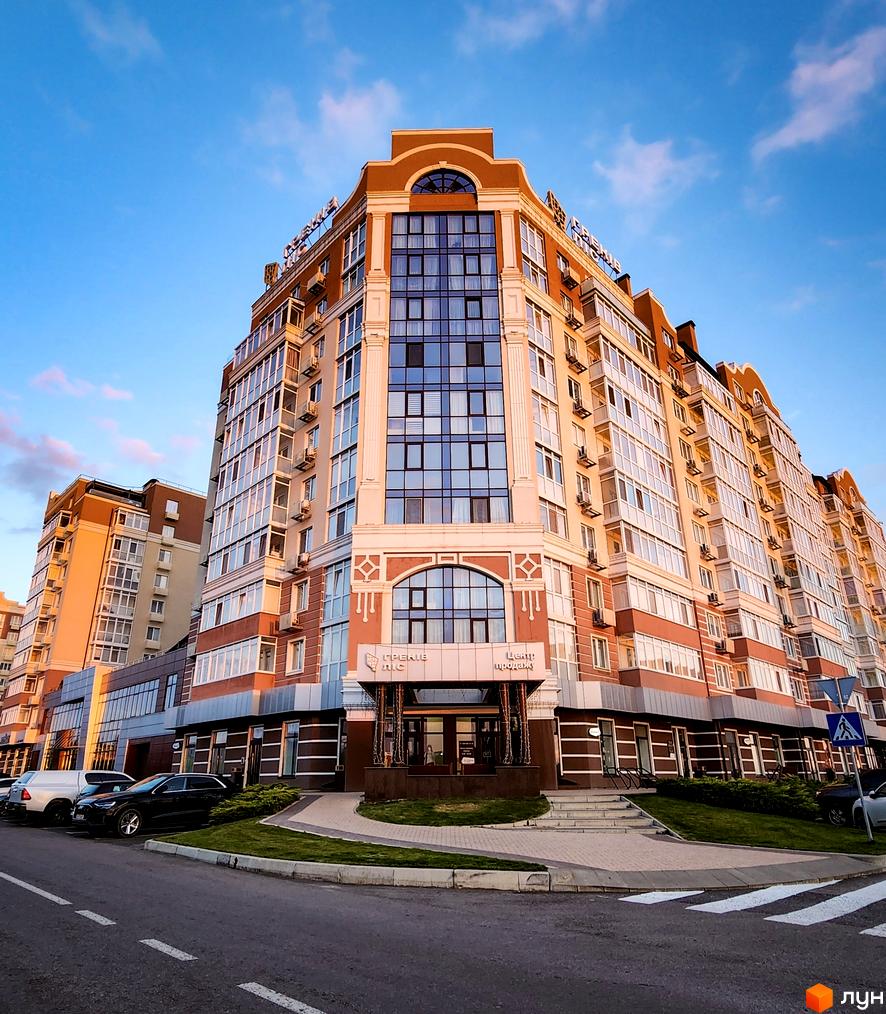 Житловий комплекс Греків Ліс - багатоповерховий будинок з великими вікнами та балконами, прибудинкова територія з доглянутим газоном та парковкою.
