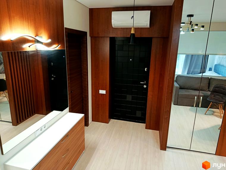 Передпокій у новобудові ЖК Вертикаль з дерев'яними панелями та дзеркальною шафою, що відбиває диван та крісло.