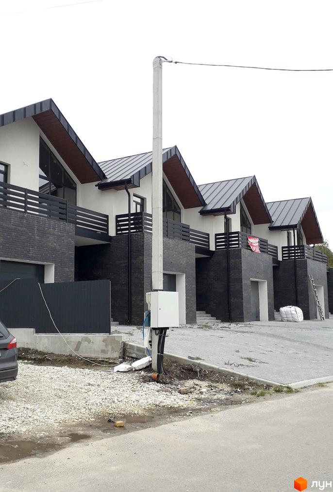 Зовнішній вигляд новобудови на вул. Набережна, 35, з темною цегляною облицовкою та сірими дахами. Прибудинкова територія з бруківкою та зеленими насадженнями.