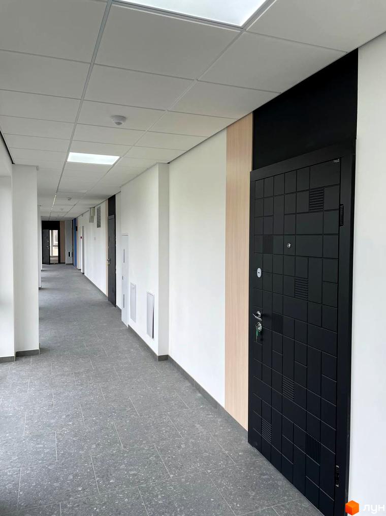 Комплекс Вертикаль: коридор з сірою плиткою на підлозі та чорними дверима. Новобудова з білими стінами та стелею.