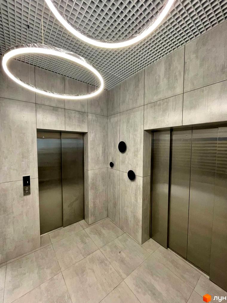 Новобудова Вертикаль: сучасний інтер'єр холу з двома ліфтами та круглими підвісними світильниками.