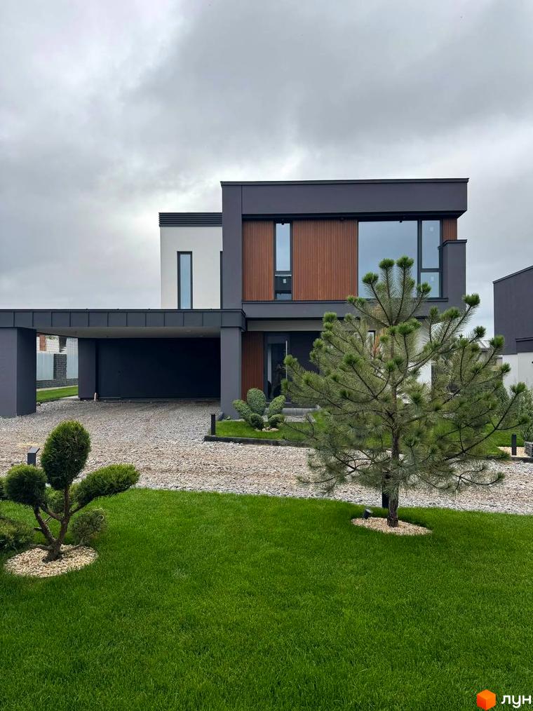 Зображення будинку в Котеджному містечку Prime Hill з дерев'яним оздобленням. На передньому плані зелений газон та декоративні дерева.