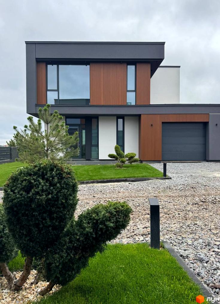 Зовнішній вигляд двоповерхового будинку з великими вікнами в Котеджному містечку Prime Hill. Навколо будинку зелений газон та декоративні кущі.